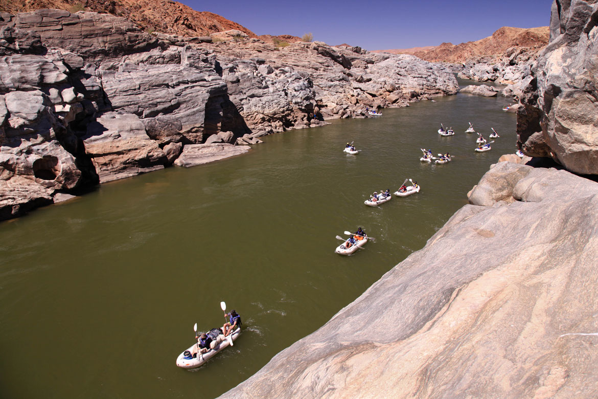 Group paddling inflatable canoes through a rocky river gorge
